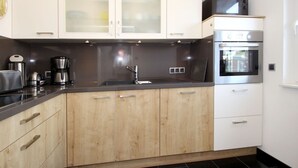 A modern kitchen with wooden cabinets, a stainless steel sink, a coffee maker, and a microwave. - Ferienhaus Wiesengrund mit Sauna, Dornumersiel (Dornum)