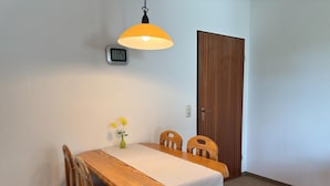 Un comedor con una mesa de madera, dos sillas, un florero con flores, un reloj de pared y una puerta.