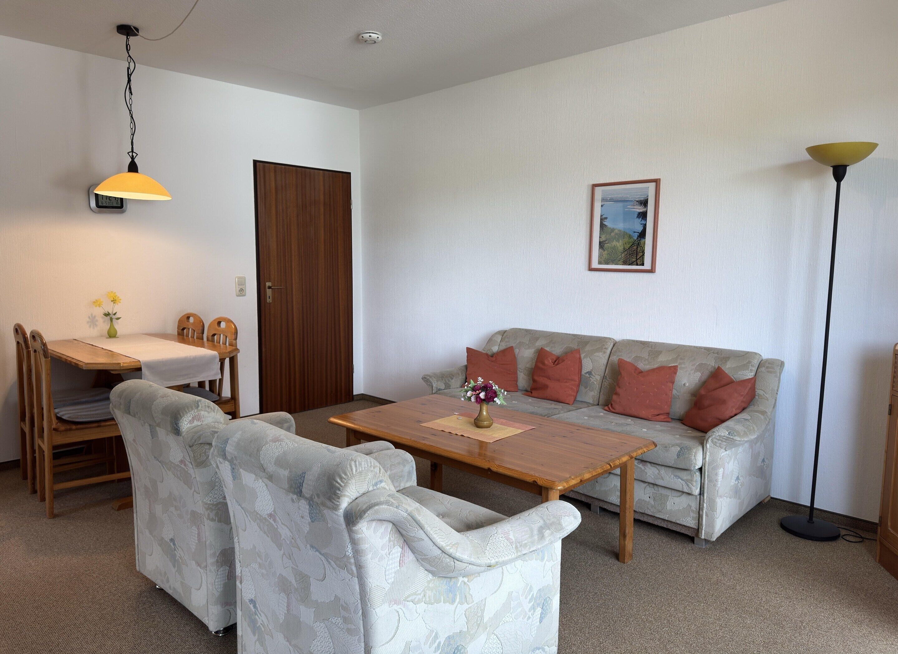 A living room with a sofa, chairs, a dining table, and a lamp.