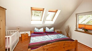 A bedroom with a sloped ceiling, two skylights, a wooden bed, a nightstand, a dresser, and a crib. - Apartment, Kenz-kustrow (Kenz-Küstrow)