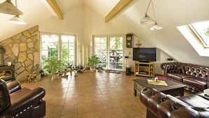 A spacious living room with a stone fireplace, leather sofas, a flat-screen TV, and large windows allowing natural light. - Apartment, Kenz-kustrow (Kenz-Küstrow)