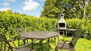 A metal outdoor seating area with a round table and chairs, a built-in grill, and a hedge in the background. - Apartment, Kenz-kustrow (Kenz-Küstrow)