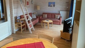 Una sala de estar acogedora con un conjunto de sofá, una mesa de centro, un televisor y una escalera apoyada en la pared.