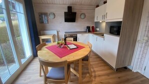 Una cocina compacta con armarios blancos, una mesa de comedor de madera y un ventanal grande.