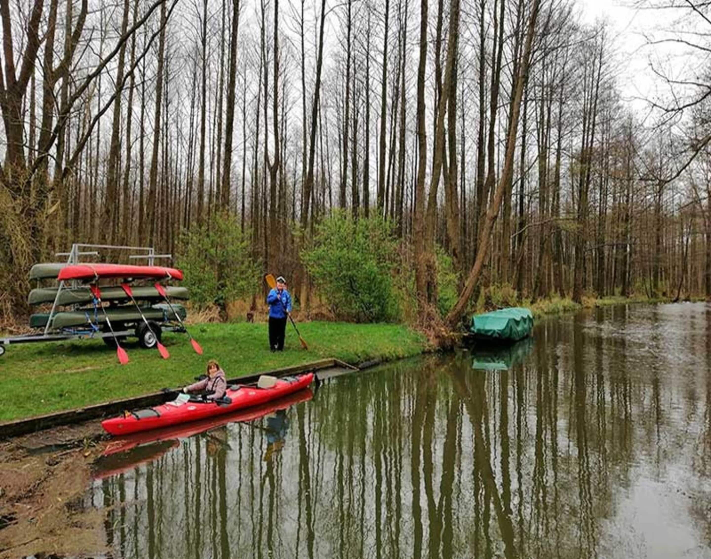 A calm river with a red canoe and a green boat docked on the bank.