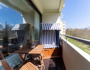 Ein Balkon mit Holztisch, zwei gestreiften Stühlen und einem Blumentopf.