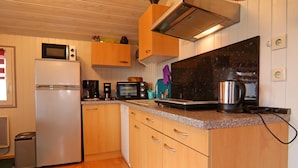 A compact kitchen with wooden cabinets, a white refrigerator, a microwave, a toaster, and a coffee maker. - Ferienhaus in Hunning an der Treene (Silberstedt)