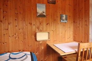 Puupaneeliseinäinen huone, jossa on sänky, työpöytä ja kaksi kehystettyä kuvaa seinällä.