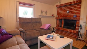 A living room with a brown sofa, a white coffee table, and a brick fireplace. - Ferienhaus in Hunning an der Treene (Silberstedt)