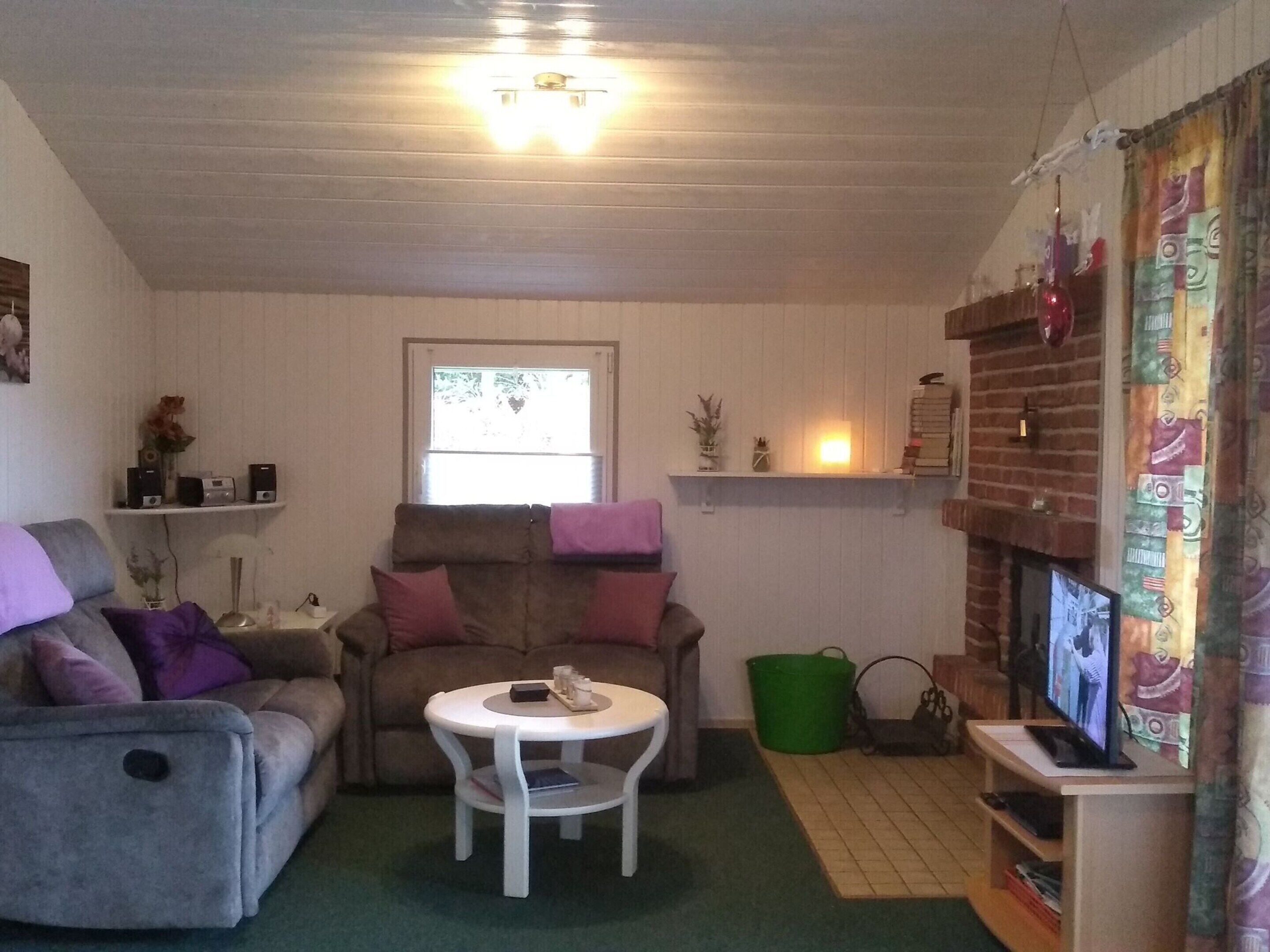 Een gezellige woonkamer met een bank, een klein rond tafeltje, een televisie en een open haard.