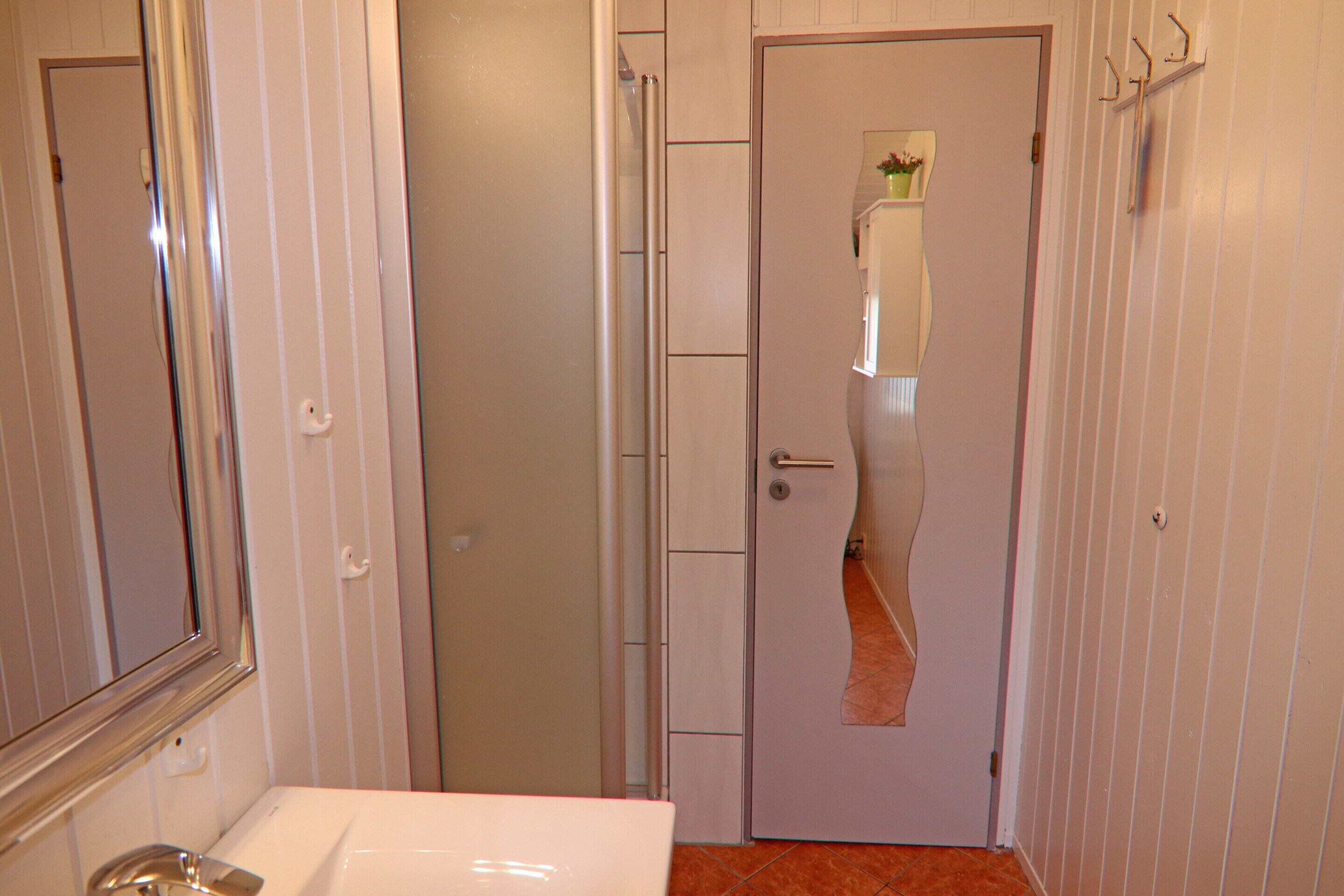 A bathroom with a white sink, a mirror, and a door leading to a hallway with a small plant on a shelf.