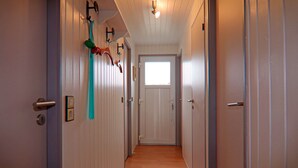 Un couloir étroit avec un plancher en bois, des murs blancs et des portes de chaque côté.