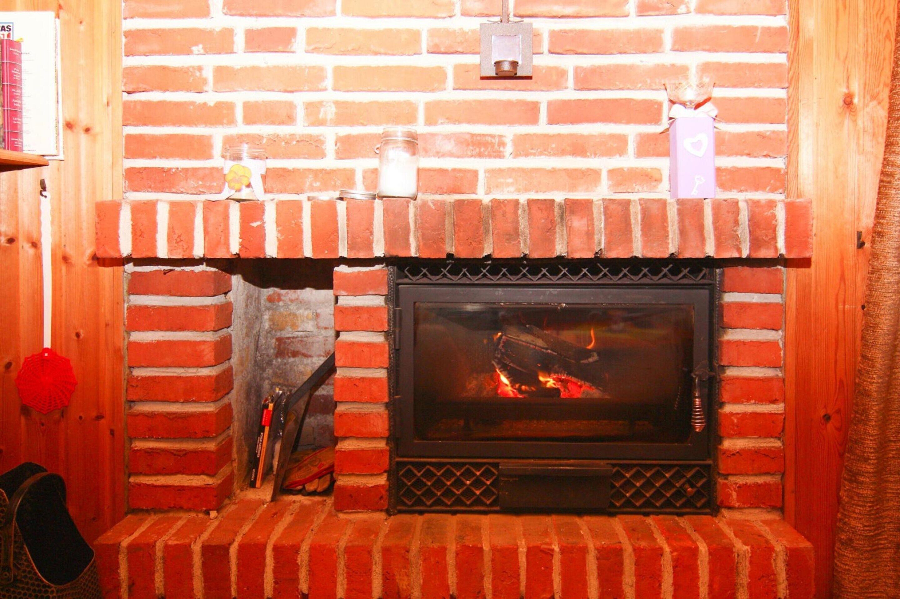 Una chimenea de ladrillo con puerta de vidrio, un estante de madera con una vela y un pequeño adorno en la pared.