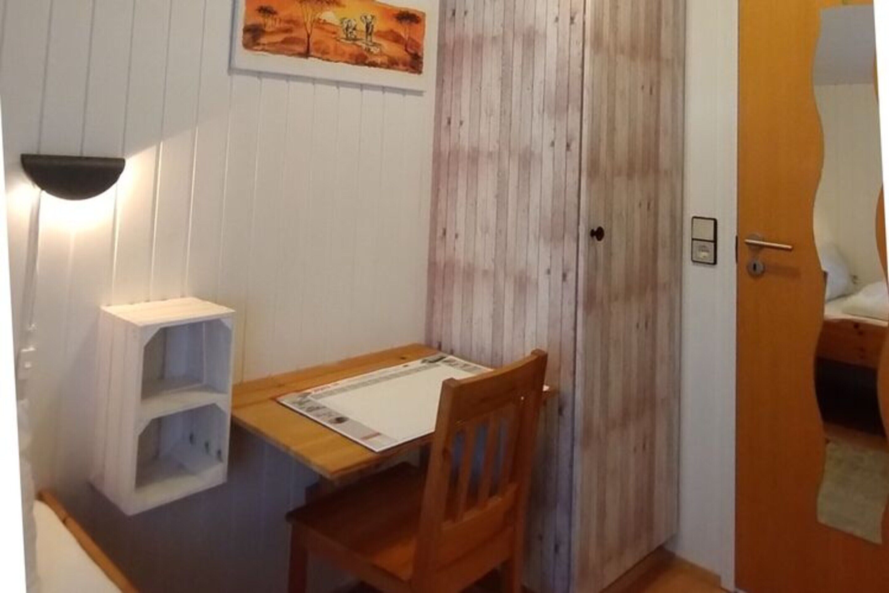 Une petite pièce avec une table et une chaise en bois, une étagère blanche et une porte avec un panneau en bois.