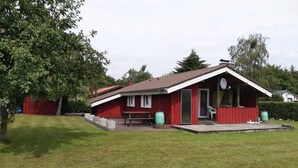 A red building with a sloped roof, a picnic table, and a covered area with a bench. - Ferienhaus in Hunning an der Treene (Silberstedt)