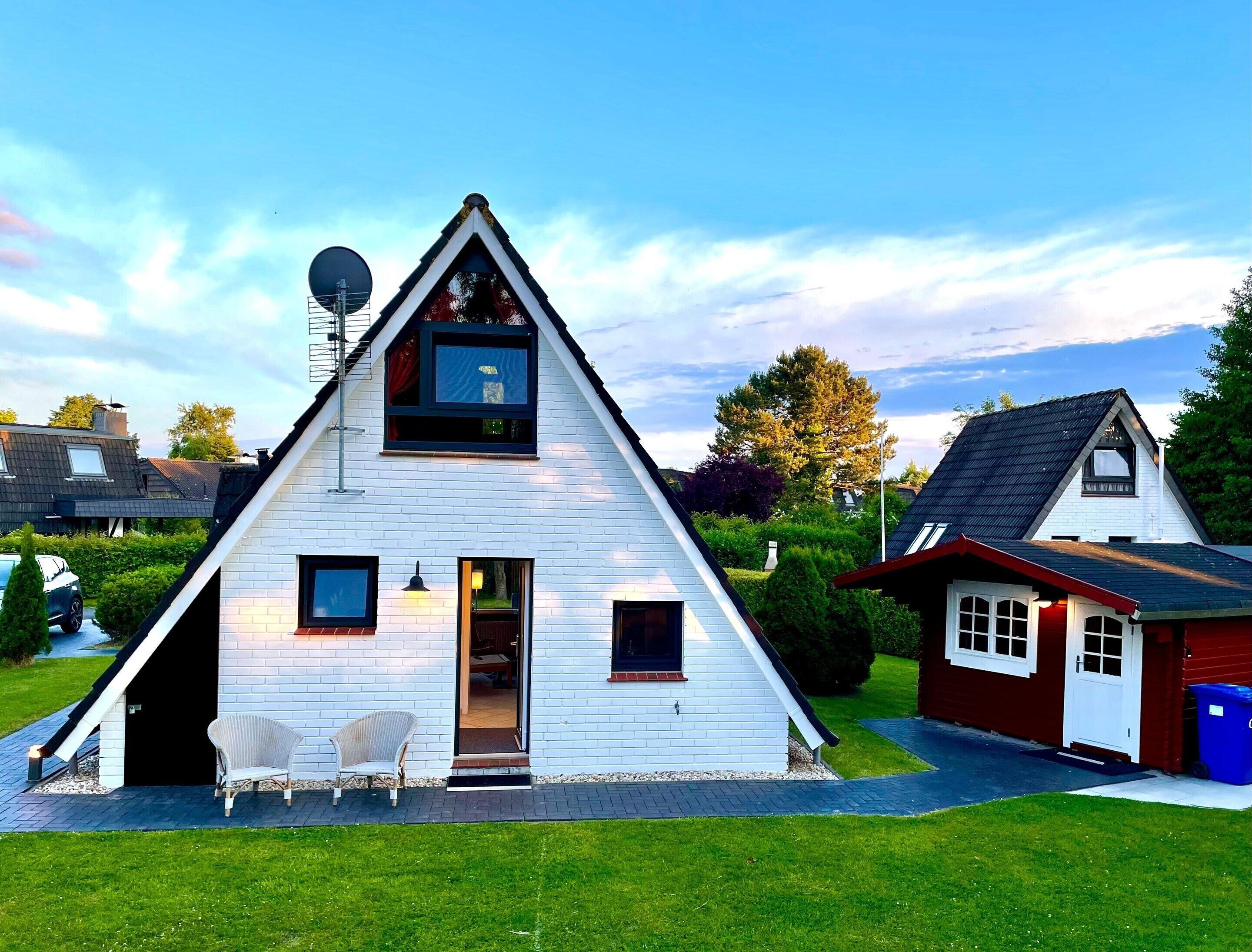 A white triangular house with a small balcony, a satellite dish, and a red door.