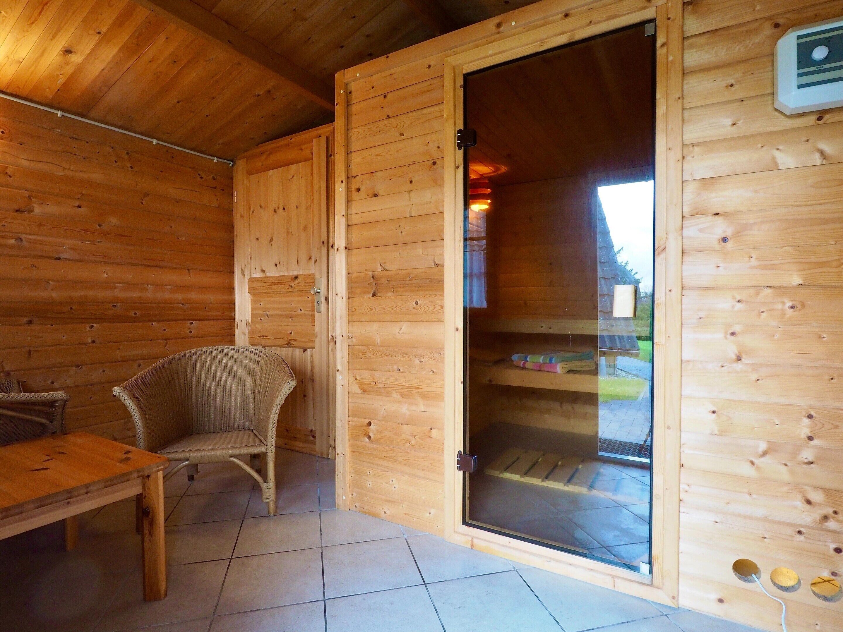 A wooden cabin interior with a dining table, wicker chair, and a sliding glass door leading to an outdoor area.