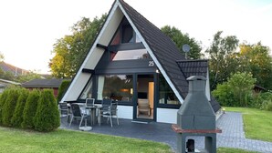 Une maison moderne avec un toit triangulaire, un patio doté de mobilier d’extérieur et une cheminée en pierre.