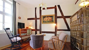 Una habitación con vigas de madera a la vista, una chimenea, una estantería y dos mecedoras.