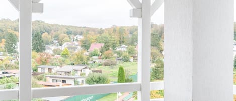 A balcony with a white railing, two wooden chairs, and a view of a residential area with houses and trees.