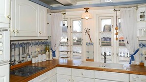 A kitchen with white cabinetry, a wooden countertop, a built-in sink, and a window with a view of a white fence and a building. - Ferienwohnung in Oevenum auf Foehr (Oevenum)