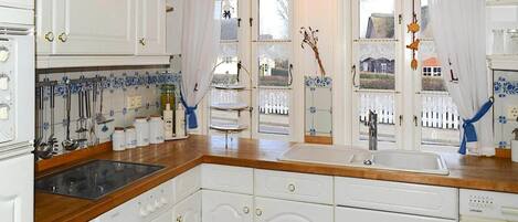 A kitchen with white cabinetry, a wooden countertop, a built-in sink, and a window with a view of a white fence and a building.