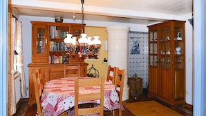 A dining room with a wooden table and chairs, a bookshelf, and a cabinet with glass doors. - Ferienwohnung in Oevenum auf Foehr (Oevenum)