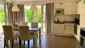 A modern kitchen with white cabinets, a microwave, and a dining area with a table and chairs. - Ferienhaus Muritzzeit in Robel an der Muritz (Röbel/Müritz)