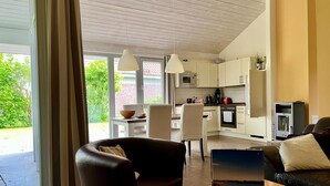 A modern kitchen with white cabinets, a dining area with a table and chairs, and a living area with a sofa and a coffee table. - Ferienhaus Muritzzeit in Robel an der Muritz (Röbel/Müritz)