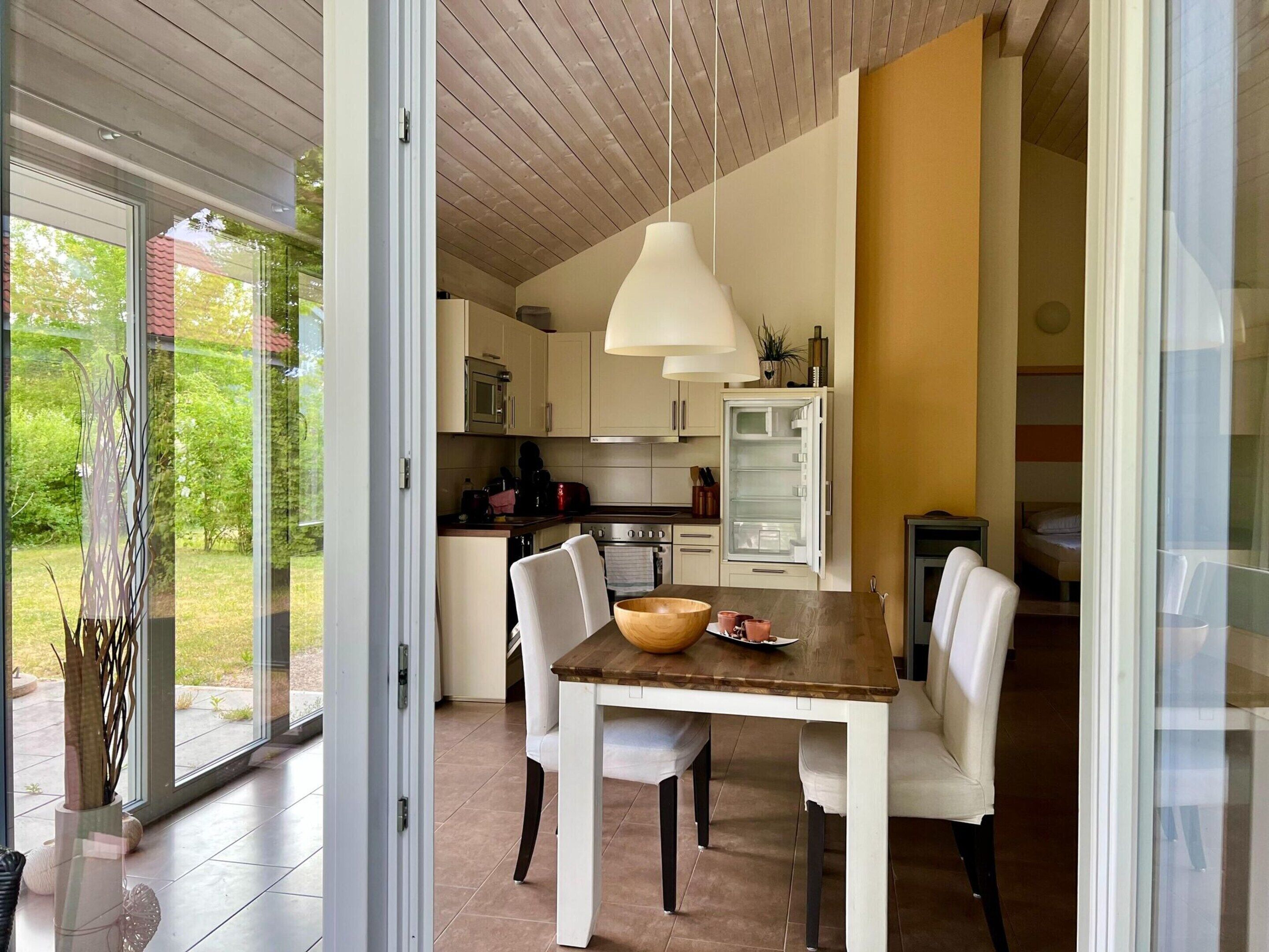 Een moderne keuken met een eethoek, met een houten tafel, witte stoelen, een hanglamp en een inbouwoven.