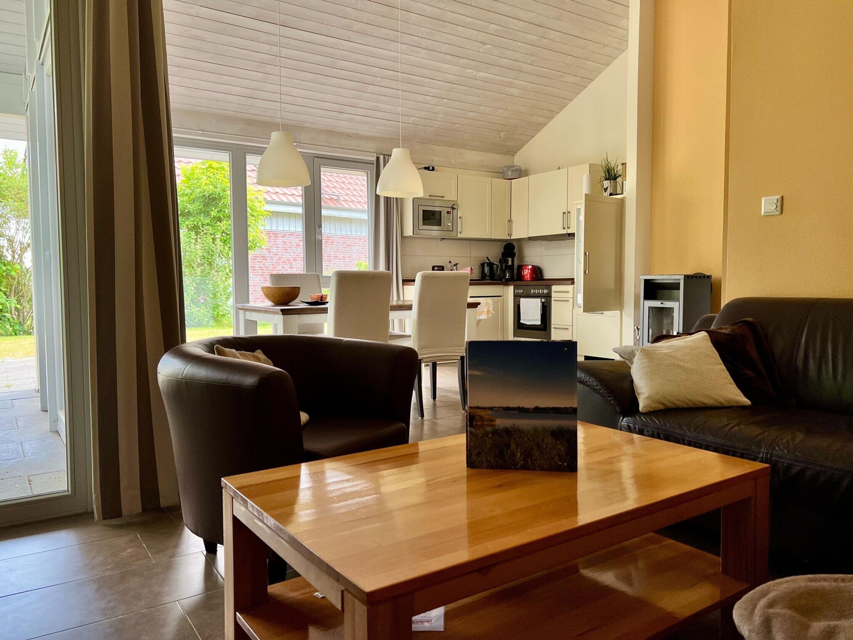 A modern living room with a wooden coffee table, a brown leather sofa, and a black leather couch. There is a dining area with a white table and chairs, and a kitchen in the background.