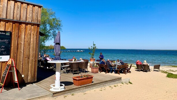 A wooden building with outdoor seating, a table, and a signboard. - Ferienhaus Muritzzeit in Robel an der Muritz (Röbel/Müritz)