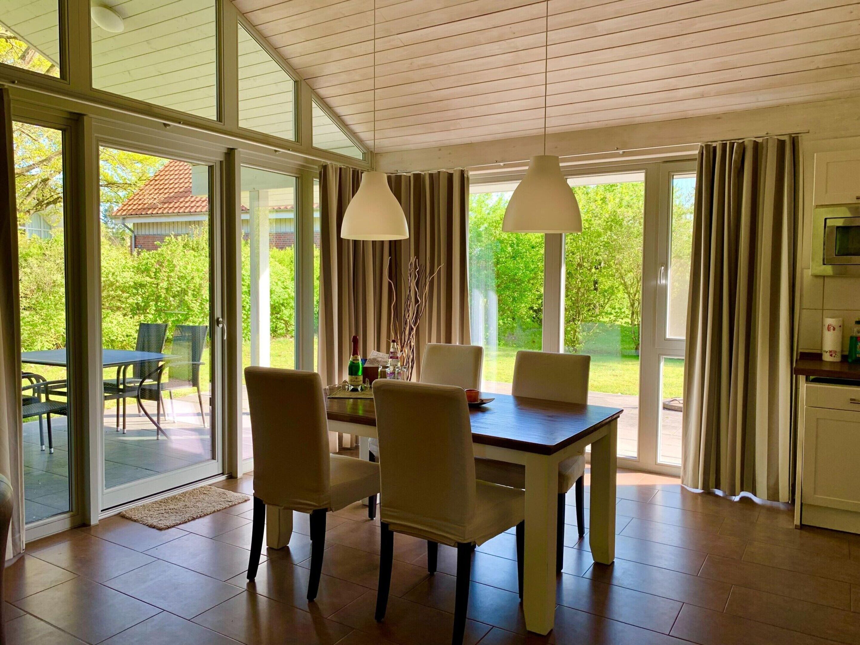 A dining area with a table and chairs, large windows, and a view of greenery outside.