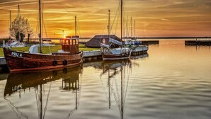 A calm harbor with boats docked at a pier during sunset. - Ferienhaus, Fuhlendorf (Fuhlendorf)