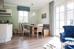 A compact kitchen with a dining area, a blue armchair, and a large window providing natural light. - Ferienhaus, Fuhlendorf (Fuhlendorf)