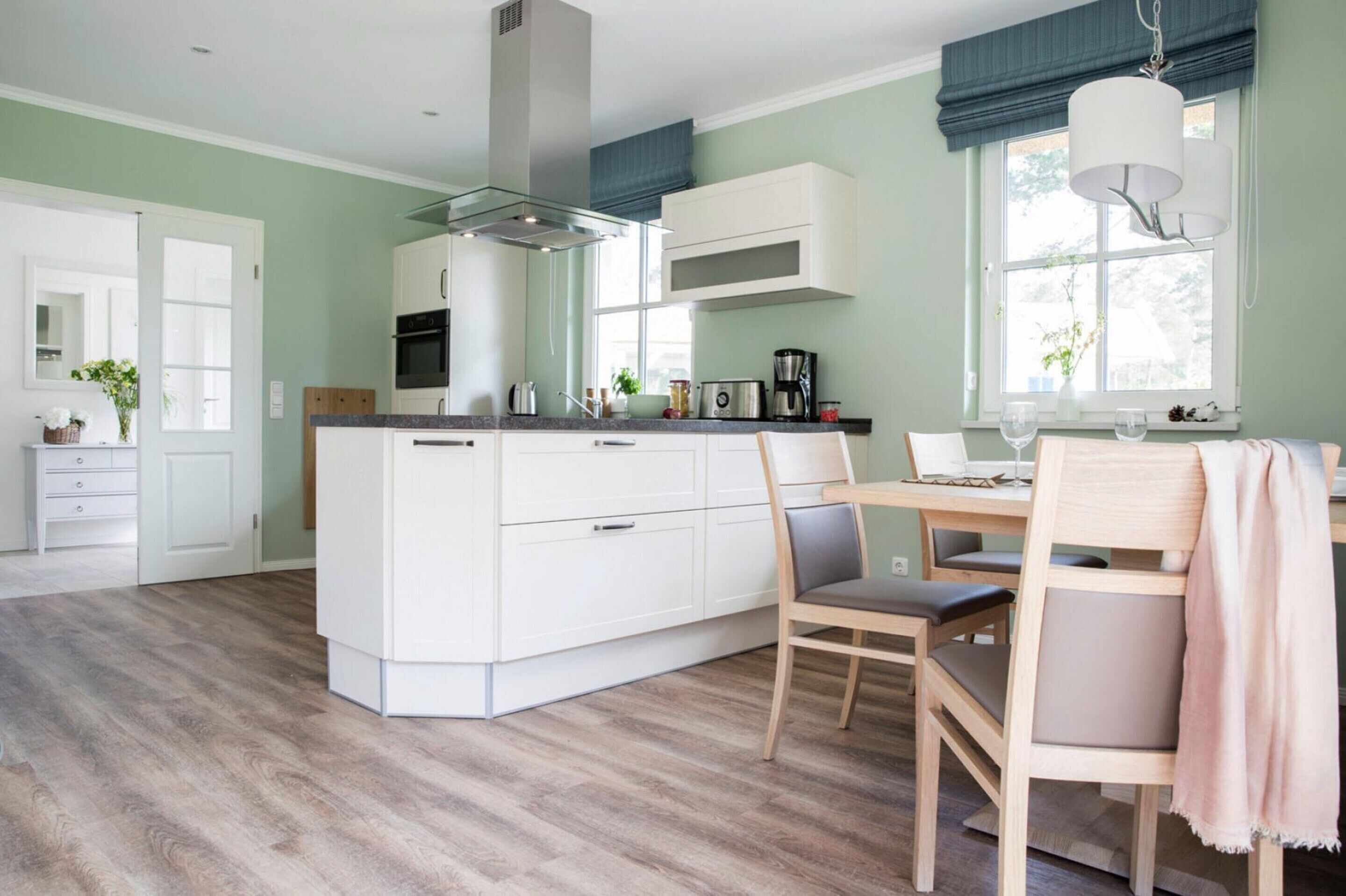 A modern kitchen with white cabinetry, a central island, and a dining area with a table and chairs.
