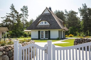 A house with a steeply pitched roof, a front porch, and a stone wall in the foreground. - Ferienhaus, Fuhlendorf (Fuhlendorf)