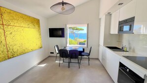 A modern kitchen with a view of the sea, a dining area with a table and chairs, and a large yellow artwork on the wall. - Luxueux Haut de Villa 4 Pers à 30m de la Plage (Sainte-Maxime)