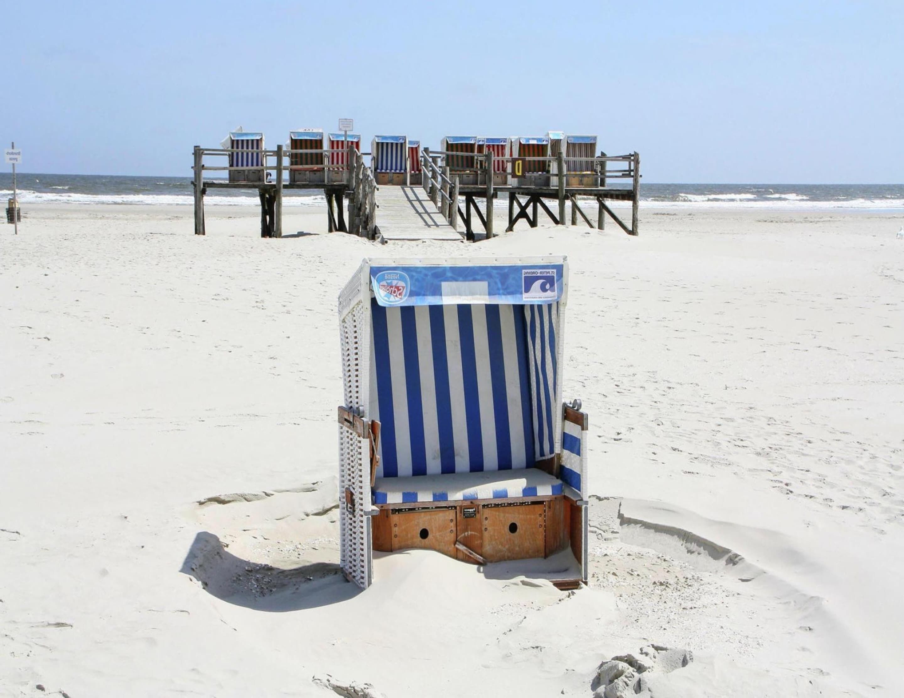 En strand med en rad strandhytter och en enda strandstol.