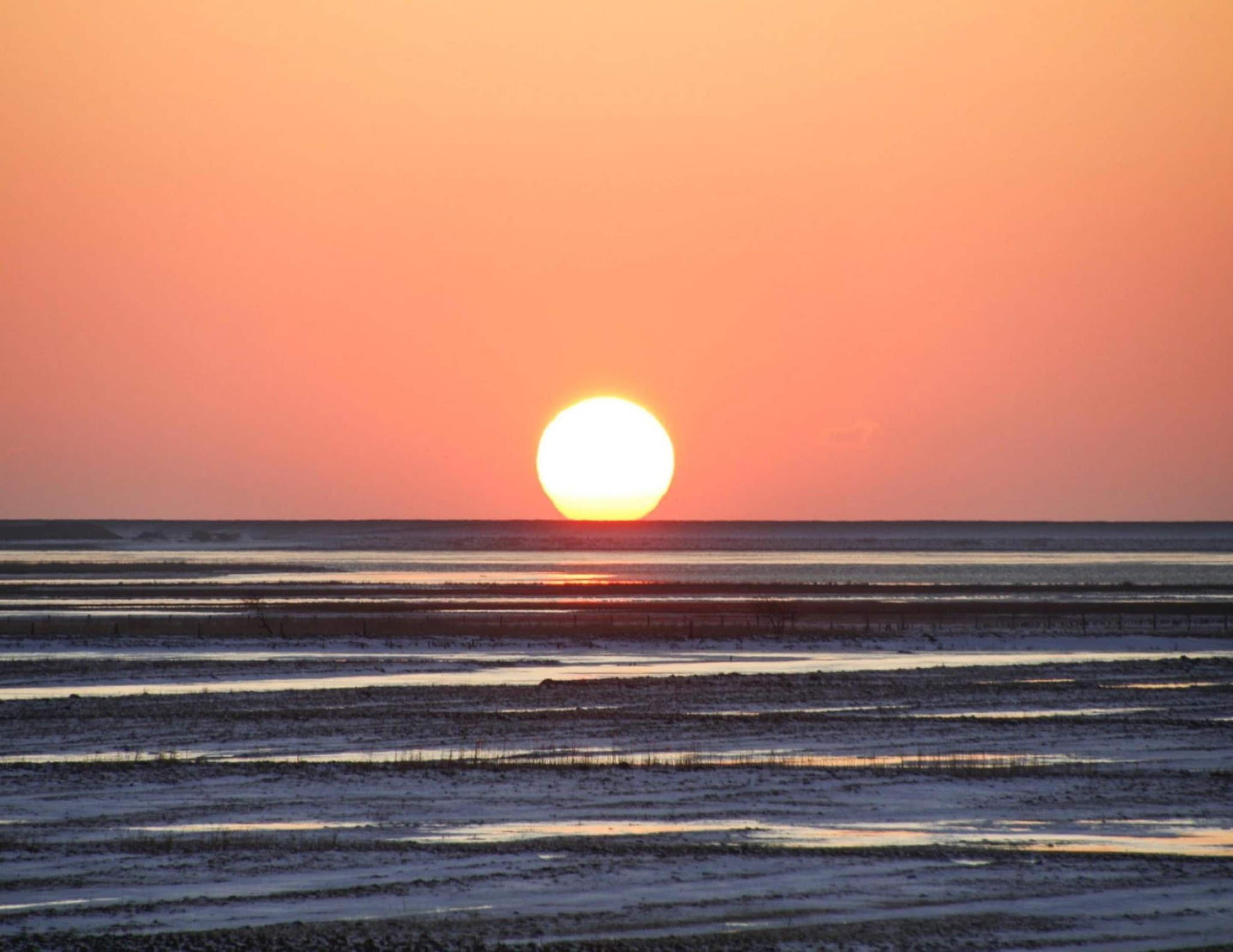 A sunset over a beach with calm waters and a clear sky.