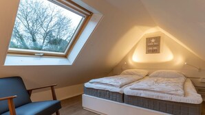 Ein Schlafzimmer mit Oberlicht, einem Bett mit zwei Kissen, einem Nachttisch und einem Sessel.