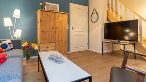 Ein Wohnzimmer mit einer Couch, einem Couchtisch mit Gläsern, einem Holzschrank, einem Fernseher auf einem Schrank und einer Treppe.