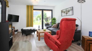 A modern living room with a red armchair, a sofa, a coffee table, and a fireplace. - Chalet Chiemgau, Inzell (Inzell)