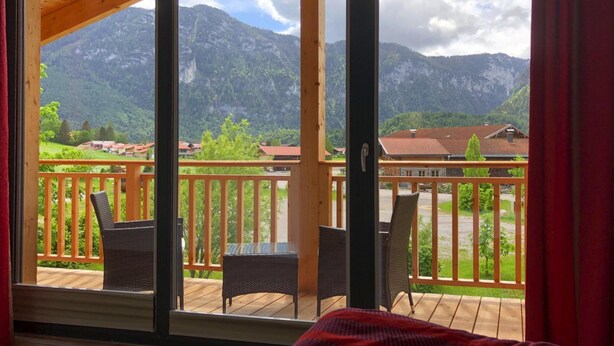 A balcony with wicker chairs and a small table, overlooking a mountainous landscape with houses. - Chalet Chiemgau, Inzell (Inzell)