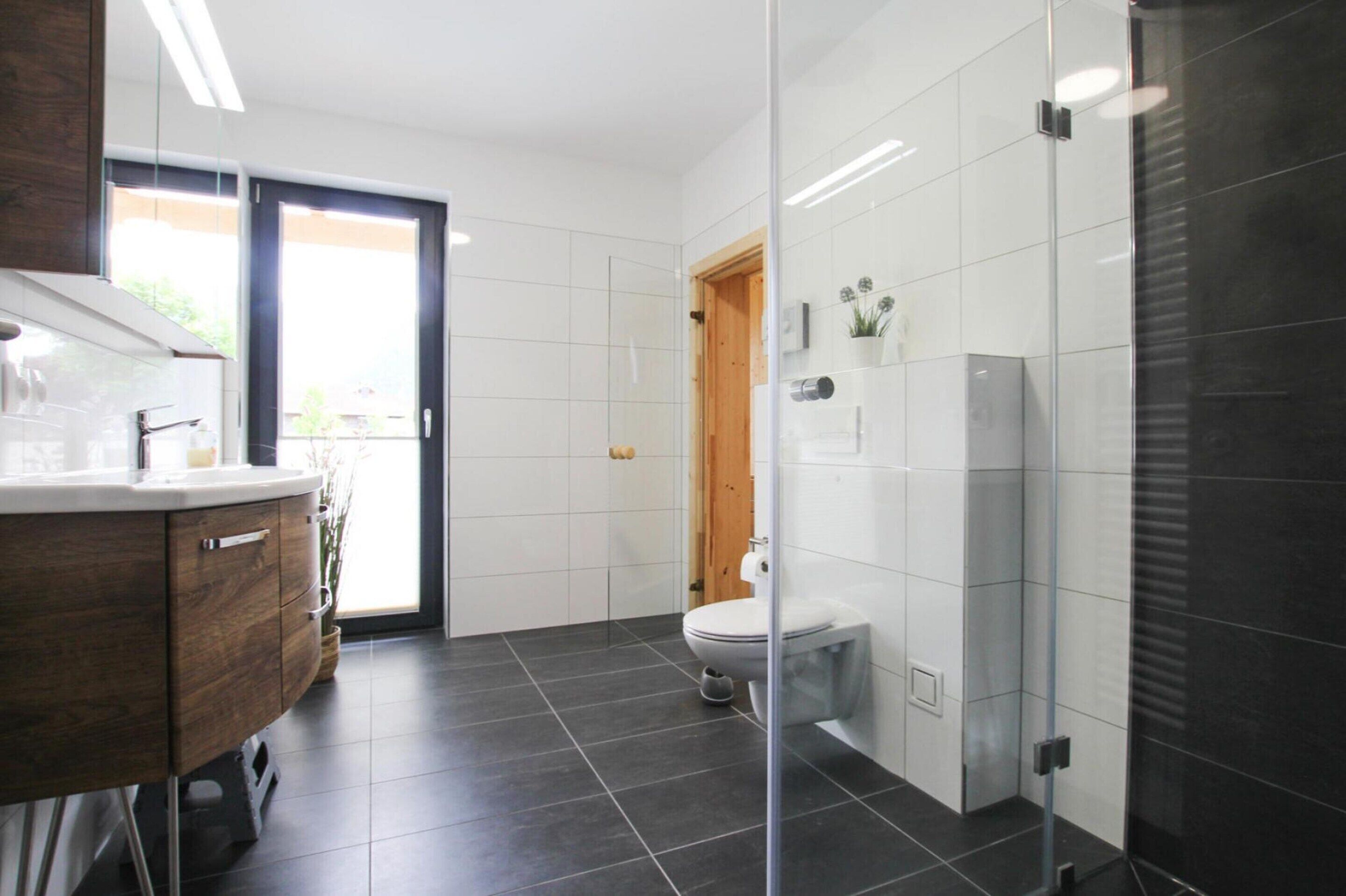 Ein modernes Badezimmer mit Duschkabine aus Glas, einer Holztür und einer weißen Toilette.