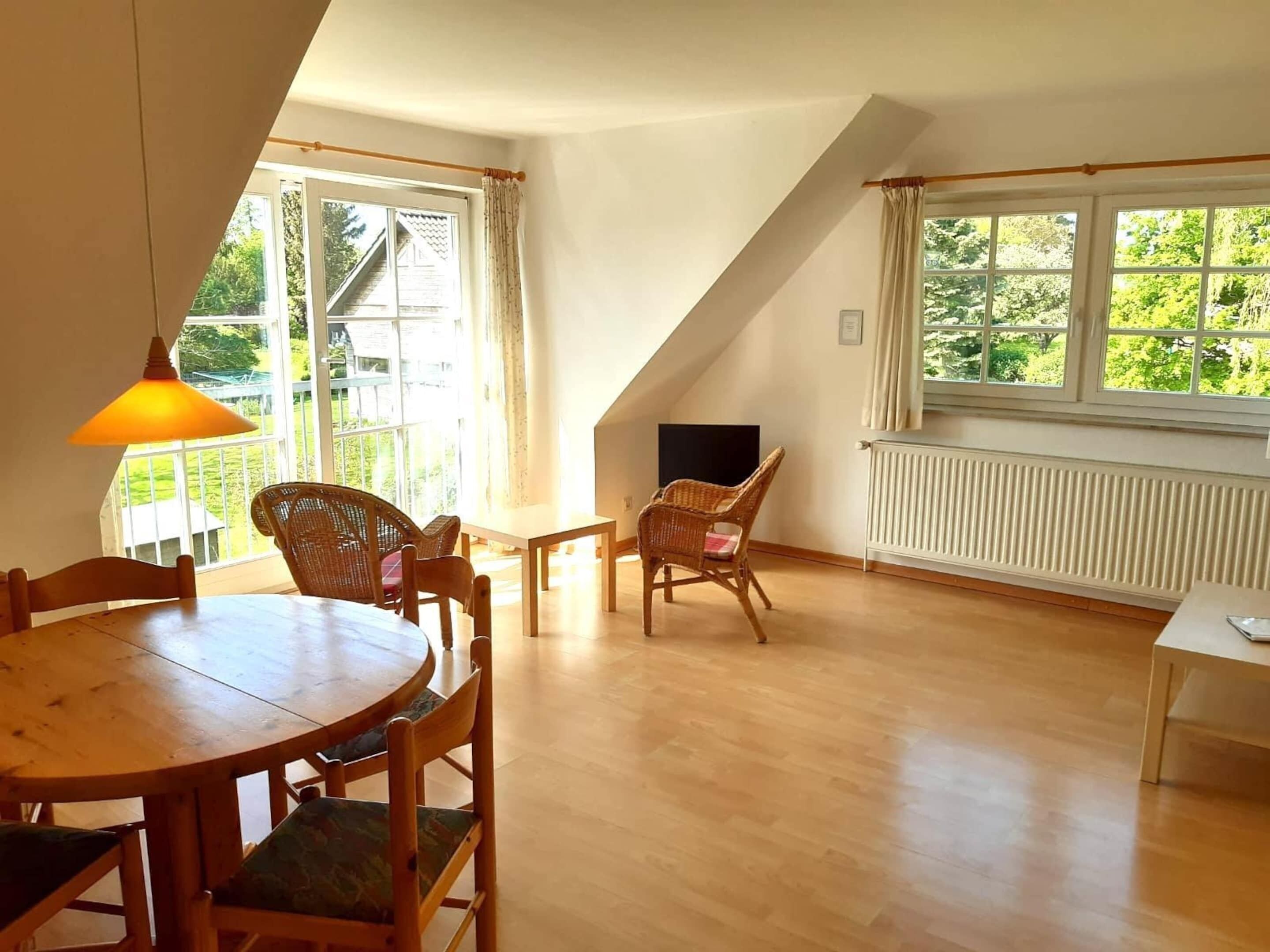 Una habitación con una mesa de comedor, sillas, un televisor y una ventana con vista a follaje.