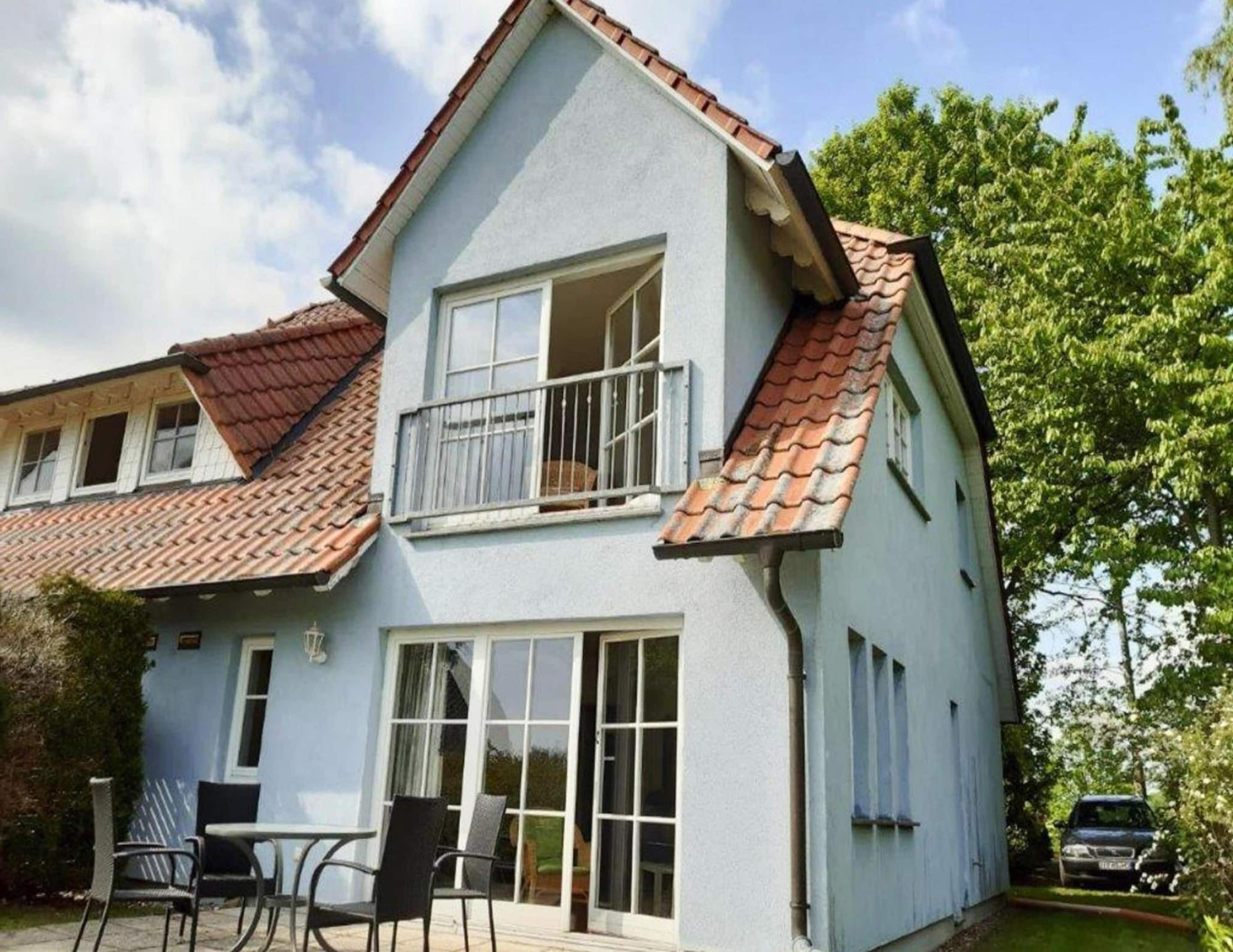 Une maison à deux étages dotée d’un balcon, de grandes fenêtres et d’un toit recouvert de tuiles.
