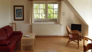 Een woonkamer met een rode bank, een houten salontafel, een rieten fauteuil en een televisie.