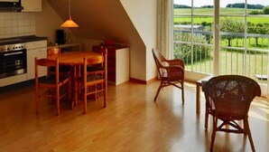 Een keuken met een eethoek, een groot raam met uitzicht op een groen landschap en een schuine kap.