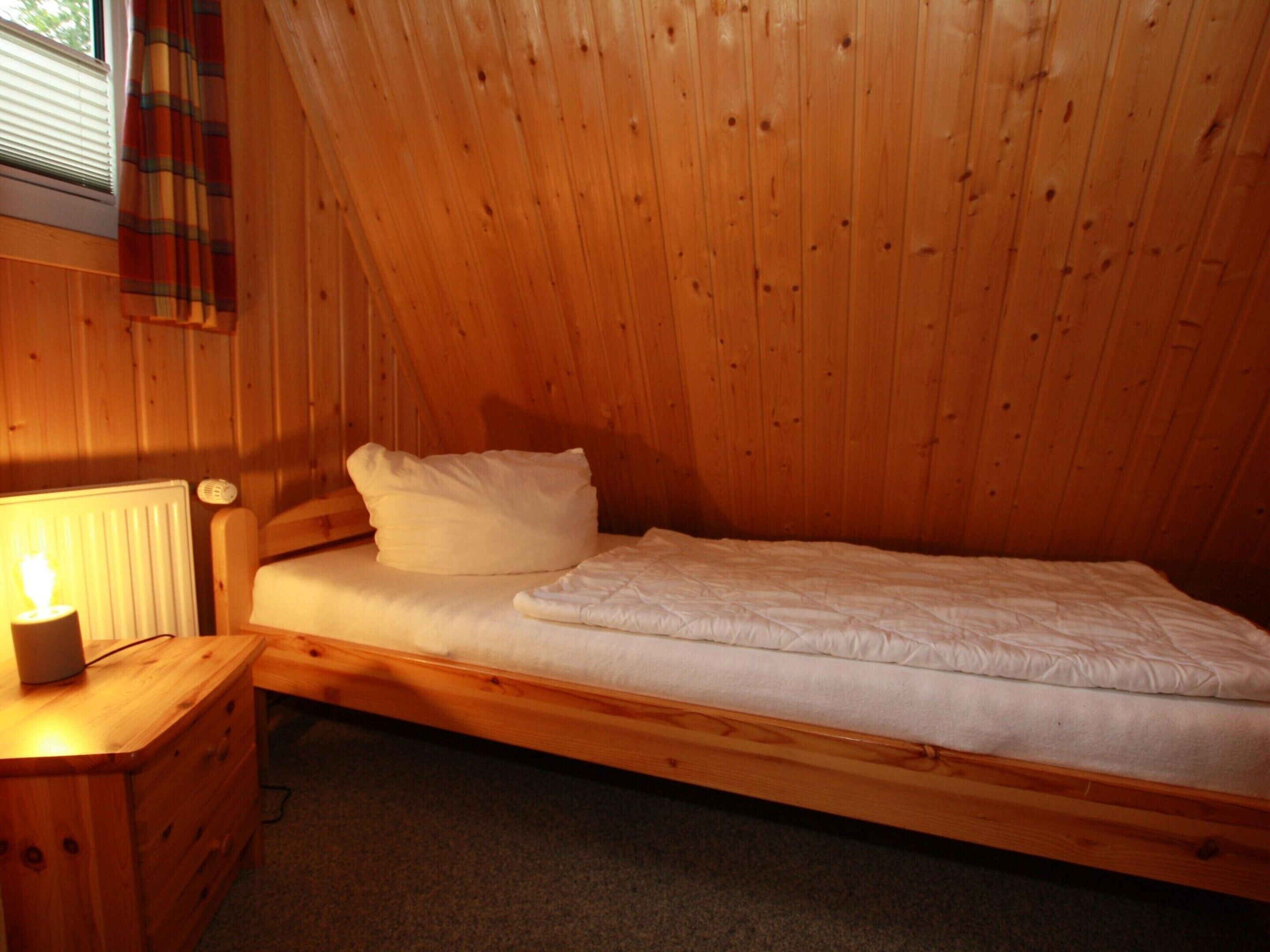 Una habitación pequeña con cama individual, paredes de madera y ventana con cortina escocesa.